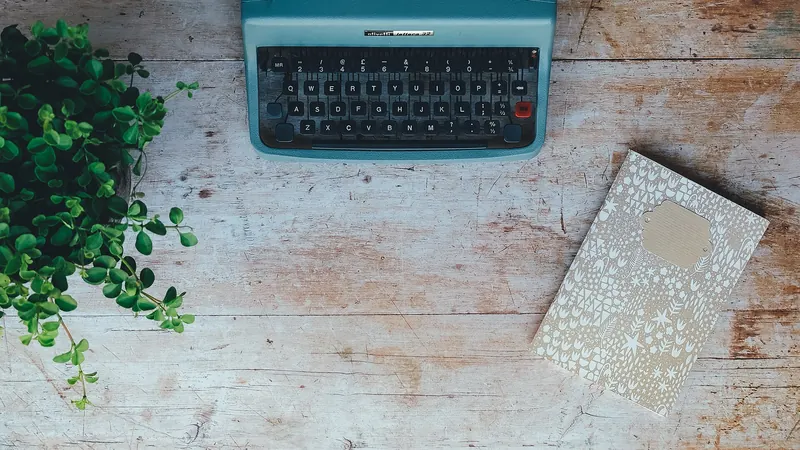 Machine à écrire bleue et carnet posés sur une table en bois clair, vue de dessus