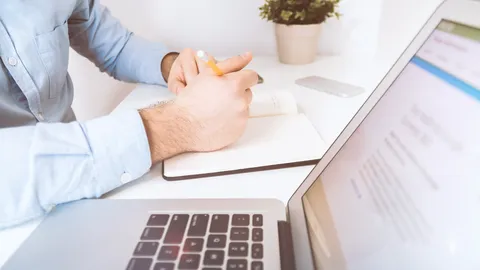 Personne qui prend des notes dans un carnet à côté d’un ordinateur portable, au bureau