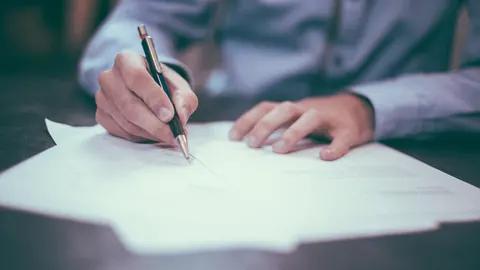 Main qui signe une feuille imprimée avec un stylo, sur un bureau