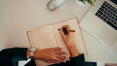 Mains qui écrivent dans un carnet à côté d’un ordinateur portable