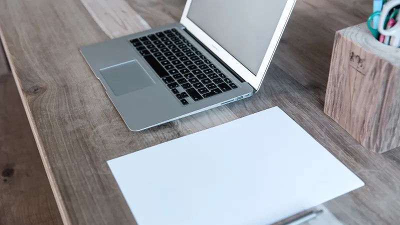 Feuille blanche posée sur un bureau en bois à côté d’un ordinateur portable