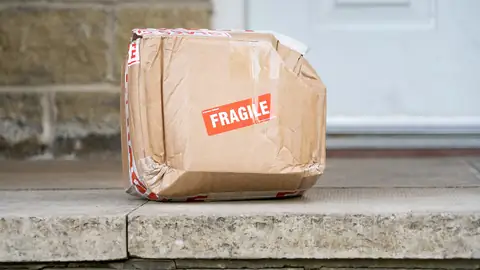 Colis en carton abîmé déposé devant une porte